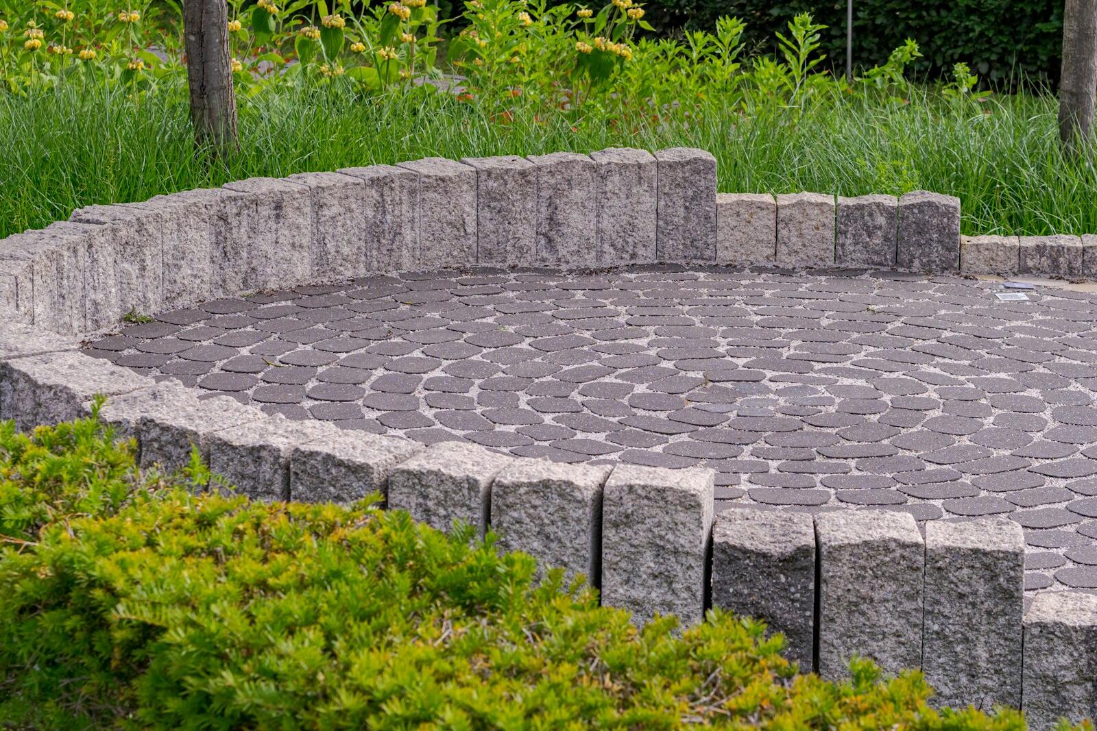 Circular paved patio edged by a low stone wall and green shrubs